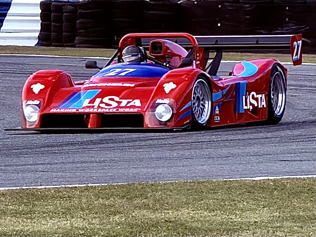 A historic open-cockpit prototype race car with a huge rear wing on track